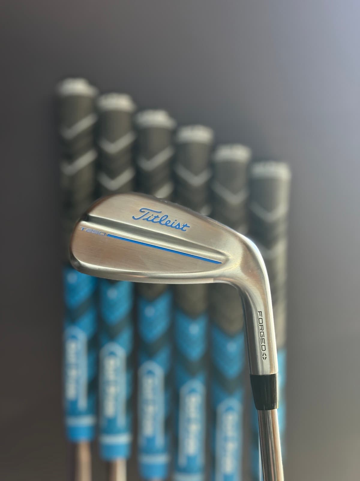 Titleist T250 iron head staged against a rack of gripped shafts